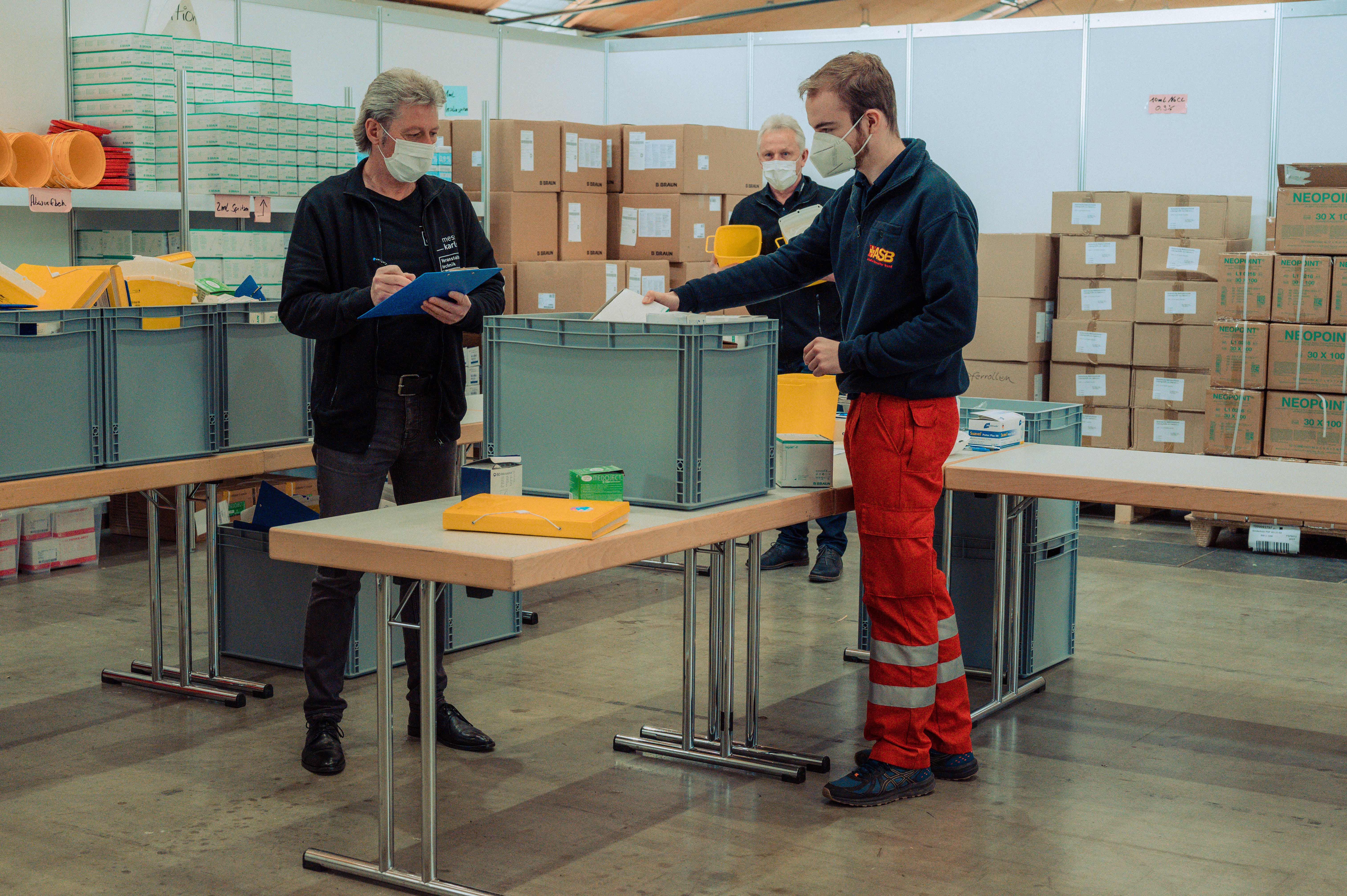 Ein DRK-Mitarbeiter sortiert mit einem Messemitarbeiter Impfmaterial Messe Karlsruhe als Impfstandort
