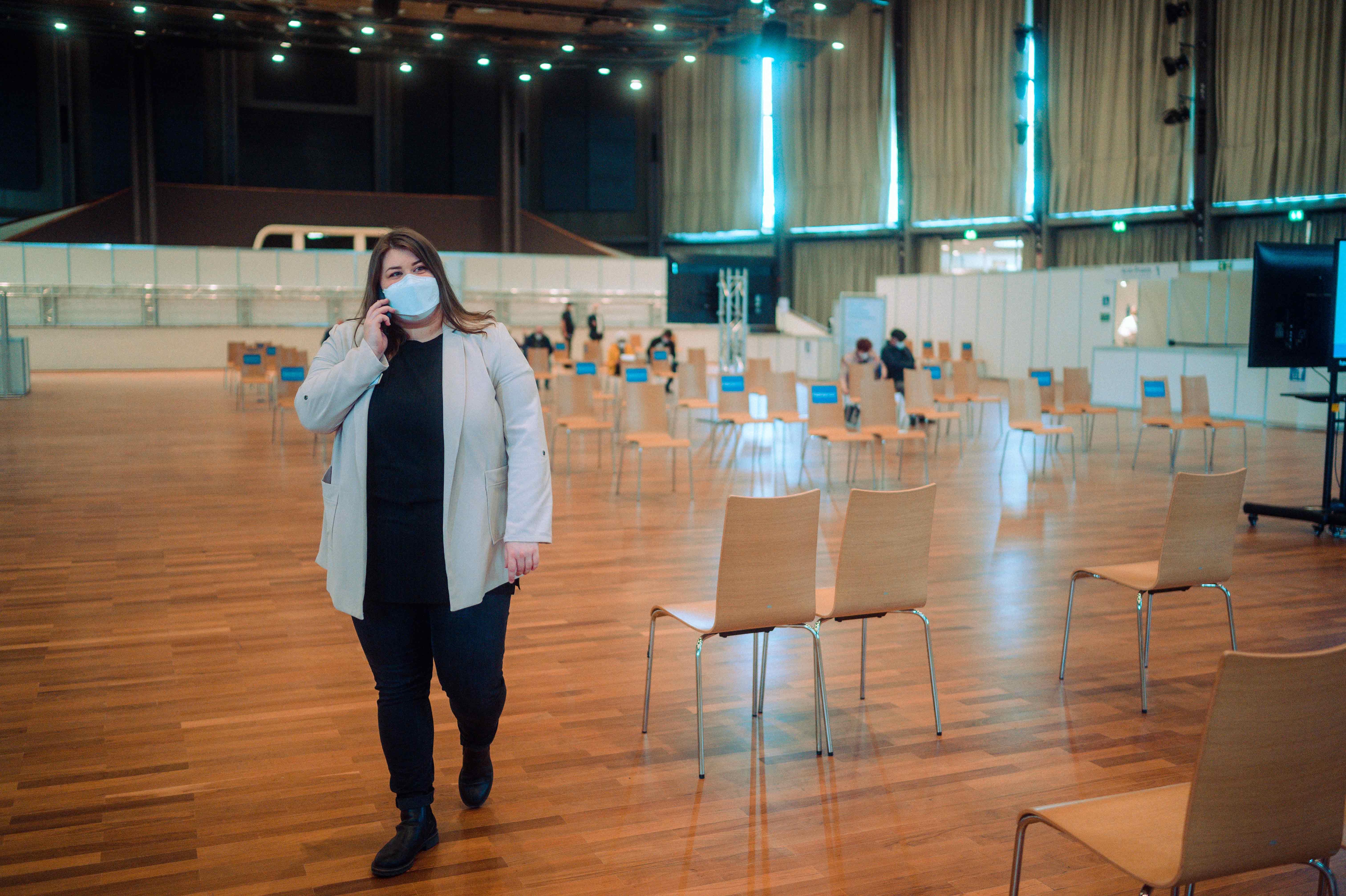 Eine Mitarbeiterin läuft durch die Halle, in der Stühle mit großem Abstand aufgestellt sind. Messe Karlsruhe als Impfstandort