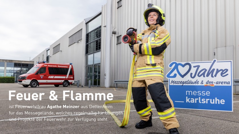 Auf dem Bild ist eine Frau zu sehen die in einer Feuerwehruniform vor dem Gebäude der Messe Karlsruhe steht und links von ihr ein Schild mir der Aufschrift, 20 Jahre Messegelände und dm-arena