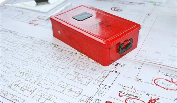 A red metal box stands on a sketched plan 