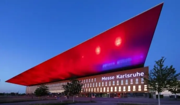 The Karlsruhe Exhibition Center building, illuminated in red and blue at night; the windows are lit up. 