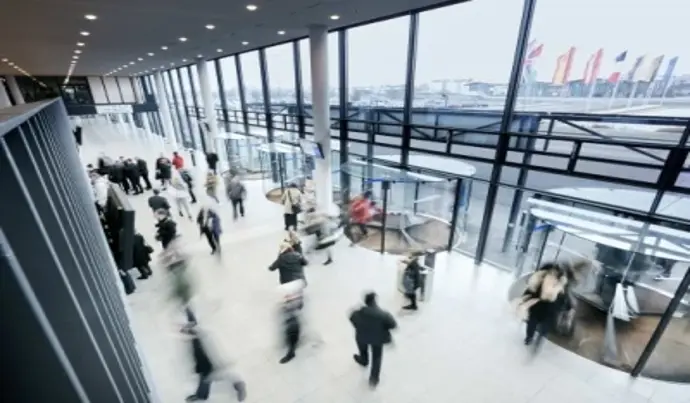 Blurred figures wander around the glass-enclosed entrance area of the Karlsruhe Exhibition Center. 