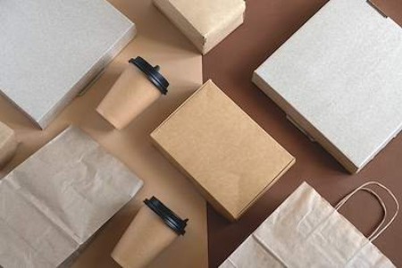 Various paper bags and cardboard coffee cups are arranged symmetrically on a brown background.