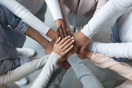 A group of people are standing in a circle with their outstretched hands placed on top of one another. 