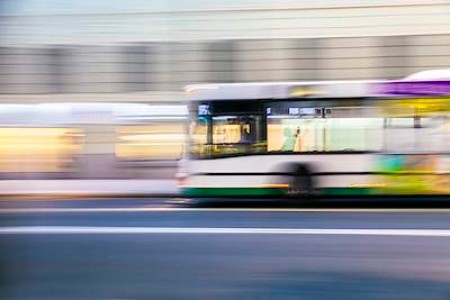 A local bus drives past a row of stores. The image isn't in focus; instead, the bus leaves a blurry trail behind it. 