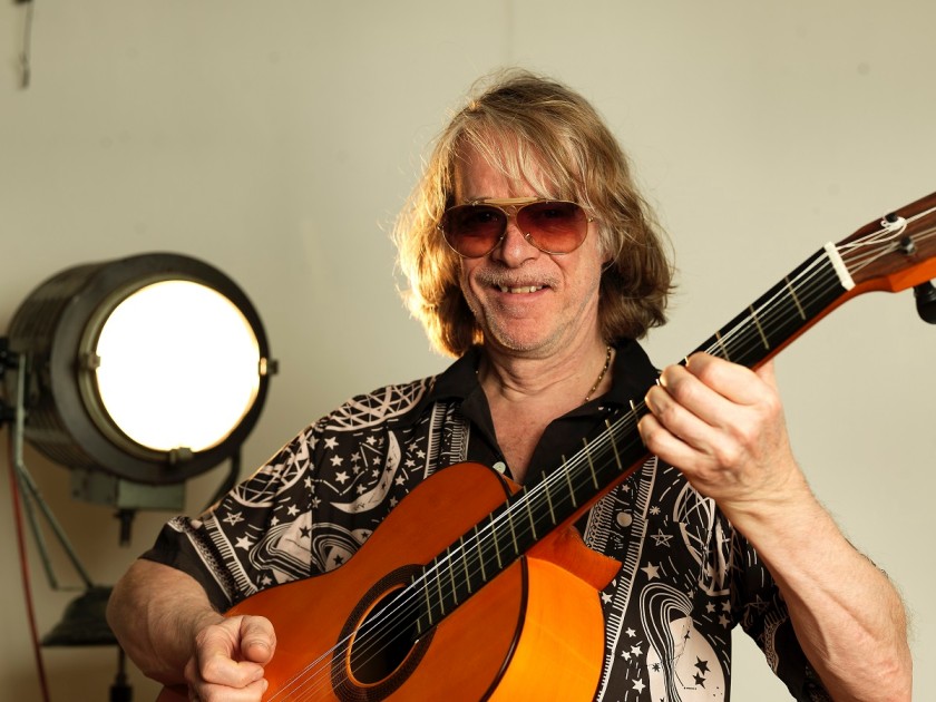 Werbebild von Helge Schneider, der eine Gitarre in der Hand hält 